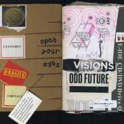 Odd future is a mixed media collage by Laura Chenault. The photo is of an open spread of my sketchbook. On the left is cardboard with stickers, a petri dish, and the text "open your eyes". There's also a fortune on cardstock hanging down. On the right is the text "visions" and "odd future over a page from an instruction manual. Pink ink circles are drown over the directions.