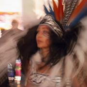 Photo from the series Dancing through the Veil by Laura Chenault. Photo features a blurry photo of a dancer wearing a feathered headdress.